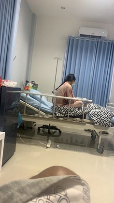 a woman sitting in a hospital bed with blue curtains