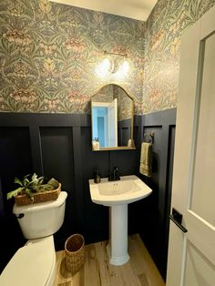 a white toilet sitting next to a bathroom sink under a mirror on top of a wooden floor