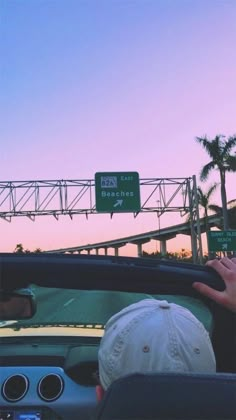 a man driving a car down a street next to a tall bridge and palm trees