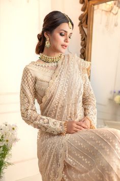 a woman in a white and gold sari is posing for the camera with her hands on her hips