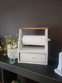 a white toilet paper dispenser sitting on top of a black table next to a vase with flowers