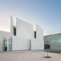 an empty courtyard in front of a building with two large white walls and one small tree