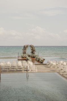 an outdoor ceremony set up on the beach with white chairs and flowers in the middle