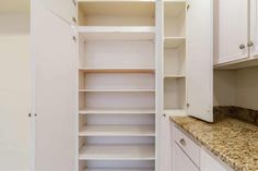 an empty pantry with marble counter tops and white cabinets