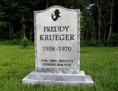 a headstone sits in the middle of a grassy area with trees and bushes behind it