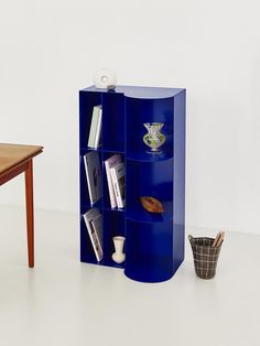 a blue book shelf sitting next to a table with a vase on top of it