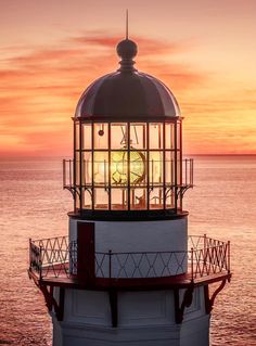 a light house sitting on top of a body of water under a cloudy sky at sunset