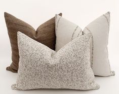 three pillows sitting next to each other on top of a white surface with one brown pillow