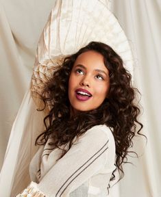 a woman with long curly hair wearing a white dress and holding a fan over her head