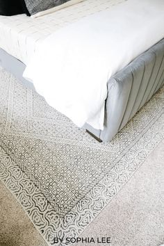 a white bed sitting on top of a carpet covered floor next to a pillow and blanket