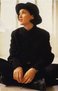 a woman sitting on the floor wearing a black suit and hat with her legs crossed