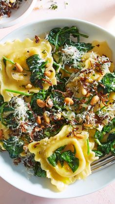 a white bowl filled with pasta and spinach covered in cheese on top of a table