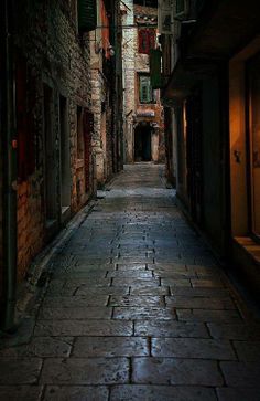 an alley way with cobblestone pavement and brick buildings on both sides at night