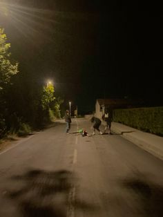 three people standing on the side of a road at night with one person falling off his skateboard