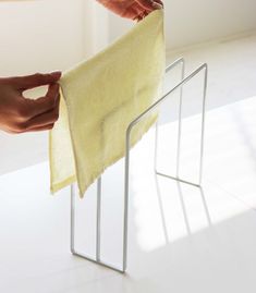 two hands are holding a yellow towel over a metal stand on a white floor, while another person is reaching for it