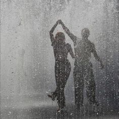 two people are standing in the rain with their hands up and one person is holding an umbrella