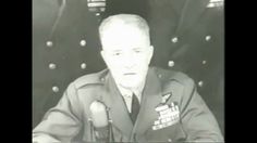 a man in uniform sitting at a table with microphones