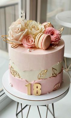 a pink and gold birthday cake with flowers on top is sitting on a white table