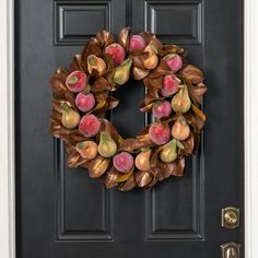 a black door with a wreath on it and apples hanging from the front, next to an open door