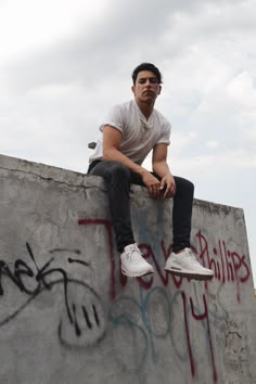 a man sitting on the edge of a concrete wall with graffiti all over his face