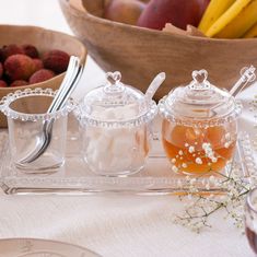 three glass containers filled with fruit on top of a table next to a bowl of strawberries