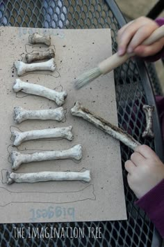 a child is drawing bones on a piece of paper with a brush and glue in front of them