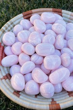 a wicker basket filled with lots of pink candy eggs on top of green grass