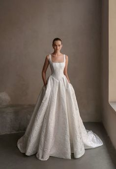 a woman in a white wedding dress standing next to a window