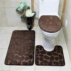 two bathroom rugs on the floor in front of a toilet and vase with flowers