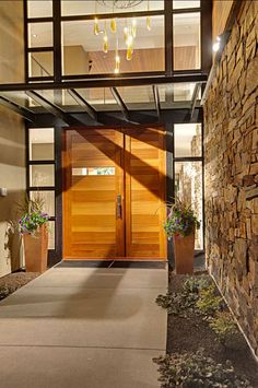 an entrance to a modern home with wood and glass doors, chandelier and potted plants