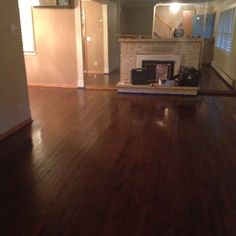 an empty living room with hard wood flooring and a fire place in the corner