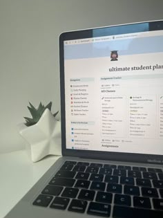 an open laptop computer sitting on top of a white desk next to a potted plant