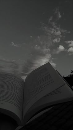 an open book sitting on top of a wooden table next to a tree and cloudy sky