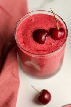 two cherries sit on top of a smoothie in a glass next to some cherries