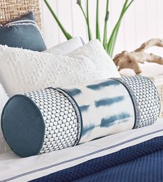 a bed with blue and white pillows on top of it, next to a plant