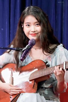 a woman holding a guitar while standing in front of a microphone