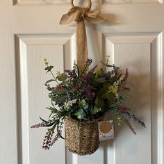 a basket hanging on the front door with flowers in it and a tag attached to the handle