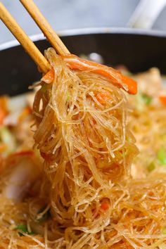 chopsticks are being used to stir food in a pan with noodles and vegetables