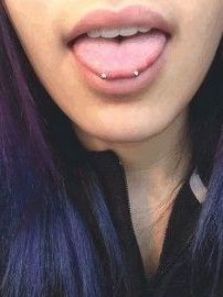 a close up of a person with purple hair and piercings on her tongue,