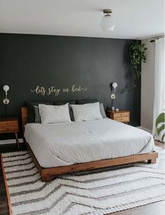 a bedroom with black walls, white bedding and rugs on the floor in front of a large window