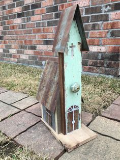 a birdhouse made out of wood sitting on the ground next to a brick wall