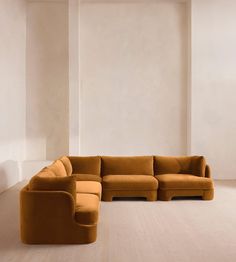 a large sectional couch in an empty room with white walls and wood flooring on the side