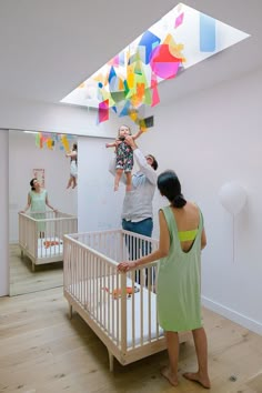 two women and a baby in a white crib with colorful streamers hanging from the ceiling