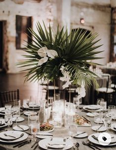 a table set with plates, silverware and palm leaf centerpieces for an elegant wedding reception