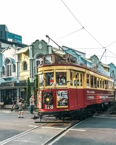 a red and yellow trolley car traveling down a street next to tall buildings with people walking on the sidewalk