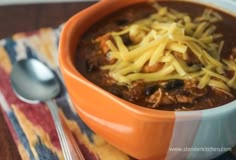 a bowl filled with chili and cheese on top of a table next to a spoon