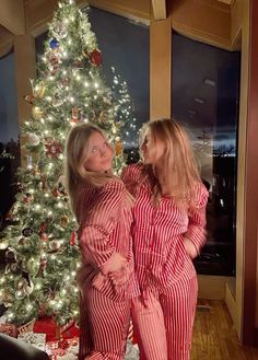 two women in pajamas standing next to a christmas tree