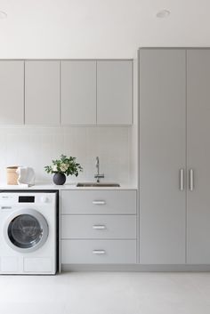 a washer and dryer in a white kitchen with cupboards on the wall