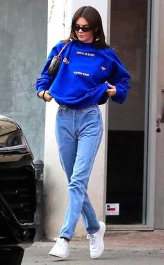 a woman in blue sweater and jeans walking down the street