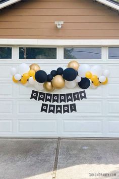 a balloon garland with black, gold and white balloons hanging from the side of a garage door